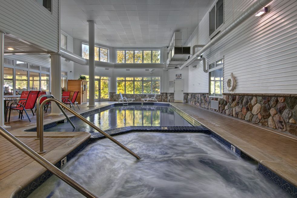 An indoor swimming pool with a handrail ladder, stone walls, and windows letting in daylight, in a leisure facility.