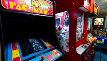 The image shows an arcade with a Ms. Pac-Man machine, a claw machine, and other arcade games in a gaming venue.