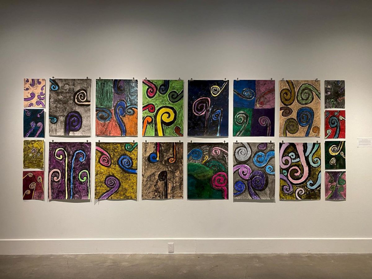 The image shows a wall with an exhibition of artworks consisting of colorful, abstract paintings featuring various spiral and swirly patterns.
