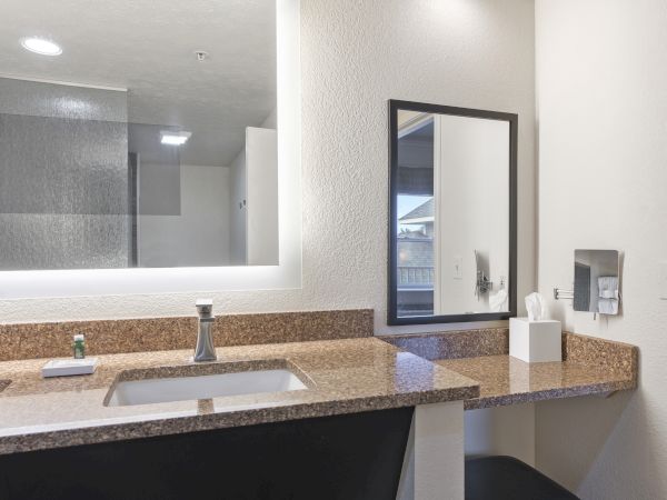 A bathroom with a granite countertop, sink, illuminated mirror, tissue box, and an installed hairdryer on the right wall ends the sentence.