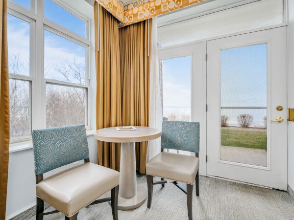 A small seating area with two chairs and a table by a window and glass door, overlooking an outdoor space.