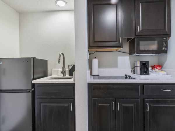 A compact kitchen setup with dark cabinets, a mini refrigerator, microwave, sink, stovetop, coffee maker, and paper towel holder on the counter.