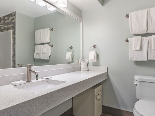 A modern bathroom with a large mirror, white countertop sink, toilet, and neatly hung towels on the wall.
