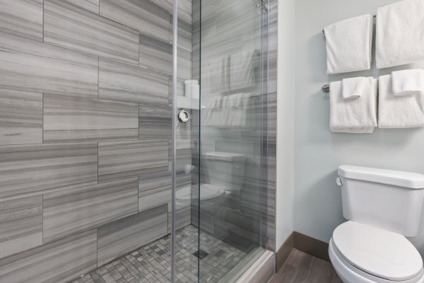 This is a modern bathroom featuring a glass-enclosed shower with grey tiles, a white toilet, and a set of towels hanging on the wall.