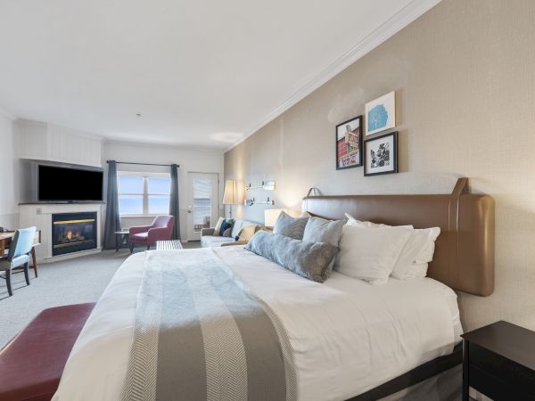 A cozy hotel room with a large bed, a fireplace, a TV, wall art, seating area by the window, and modern decor, creating a relaxing ambiance.