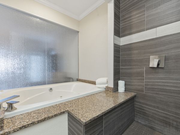 A modern bathroom features a large bathtub with a granite countertop, adjacent to a tiled shower area with a glass screen for privacy.