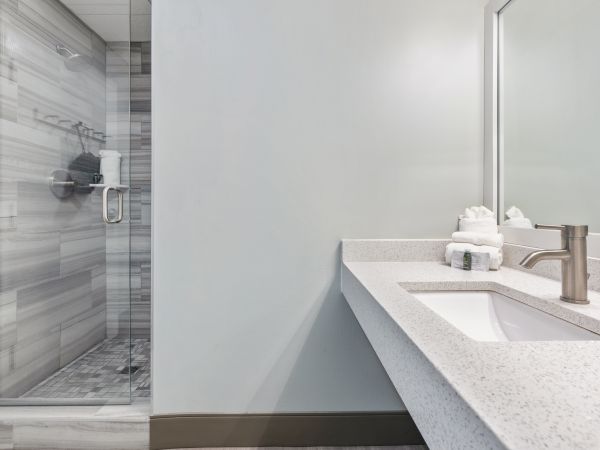 The image shows a modern bathroom with a glass-enclosed shower, a countertop with a sink, a faucet, and neatly arranged towels.
