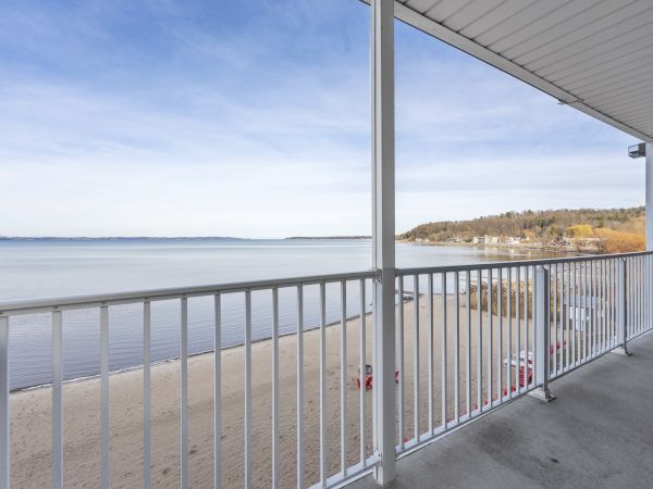 A balcony view overlooking a sandy beach and calm sea, with a railing in the foreground and a clear sky above.