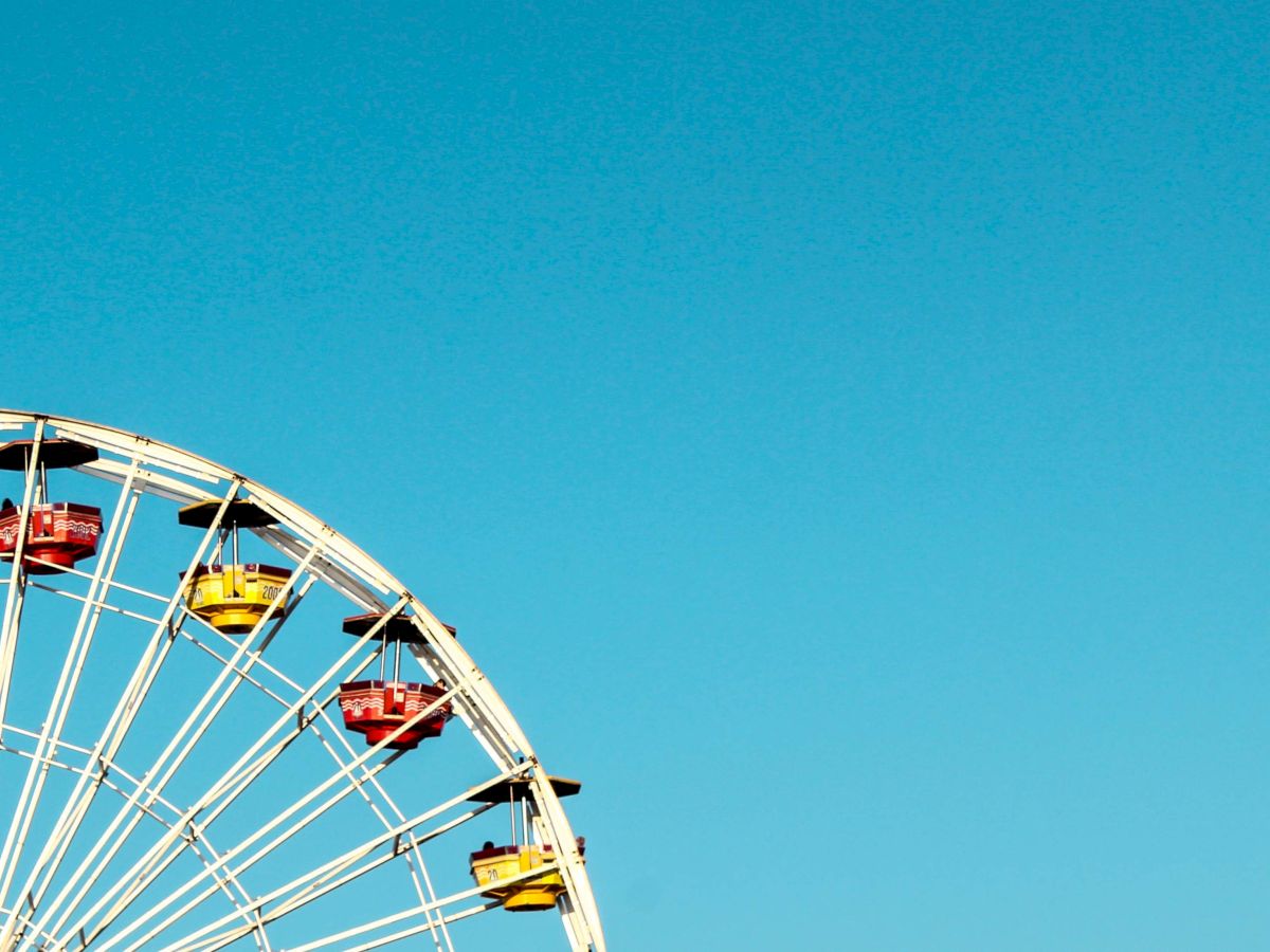 The image shows a partial view of a Ferris wheel against a clear blue sky, with red and yellow gondolas.