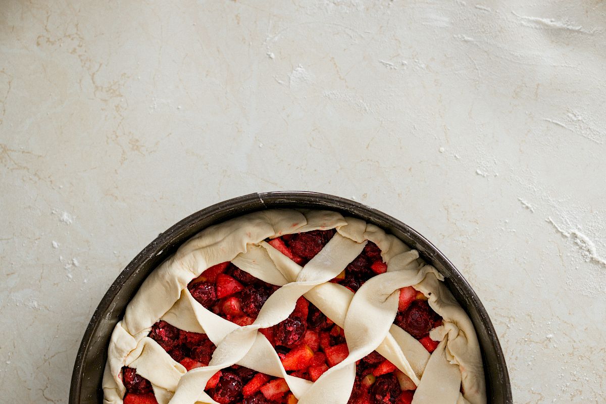 A fruit pie with a lattice crust in an unbaked state, placed on a light-colored surface.