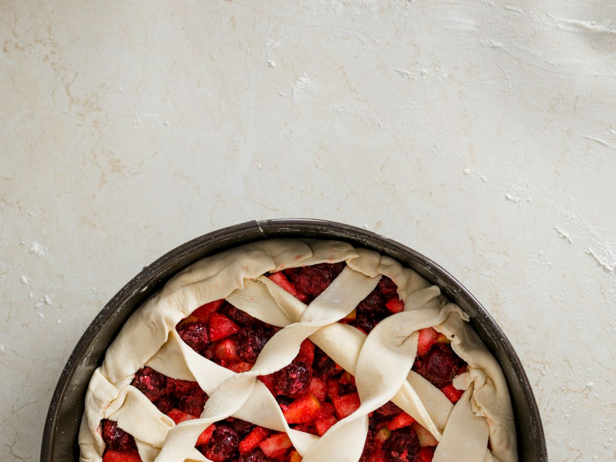 A fruit pie with a lattice crust in an unbaked state, placed on a light-colored surface.