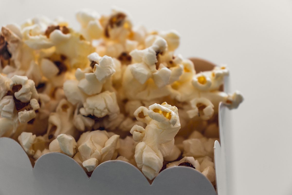 The image shows a close-up of freshly popped popcorn in a white cardboard container.