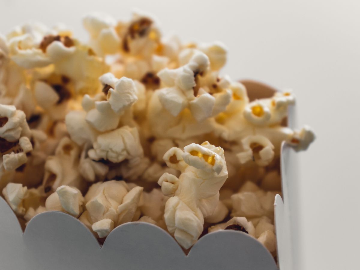 The image shows a close-up of freshly popped popcorn in a white cardboard container.