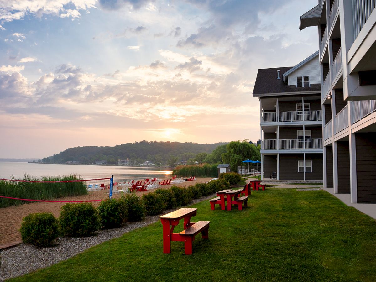 A beachside hotel with grassy lawn, red benches, and a shoreline at sunset, inviting a calm seaside stay.