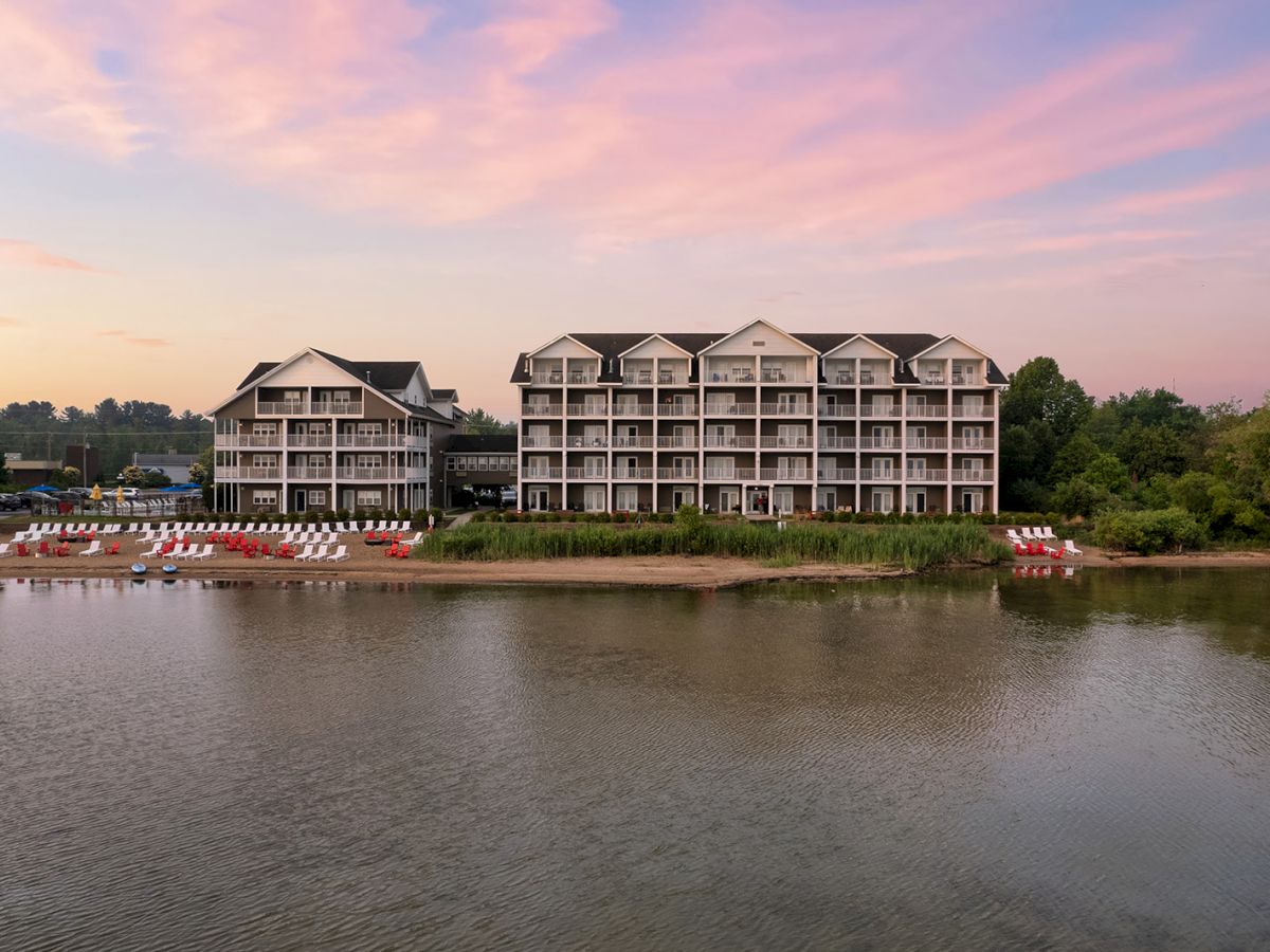 A lakefront resort with multi-story buildings, boats along the shore, and a calm water reflection at sunset.