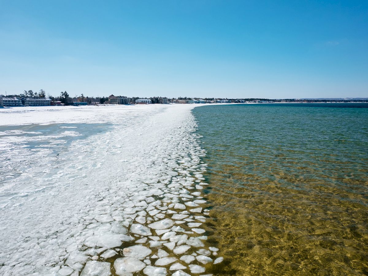 An ice-covered shoreline meets a clear body of water, with a blue sky overhead.