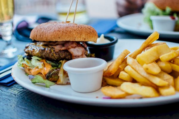A plate of food featuring a burger with toppings, a side of fries, and dipping sauces is shown on a table.