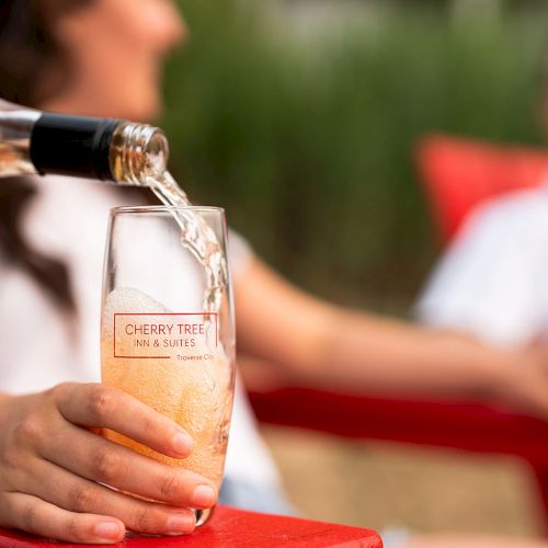 Two people at a bar or party; one is holding a beer bottle, the other sits in the background, smiling.