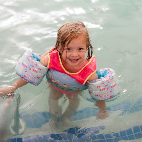A child in the water wears inflatable arm floaties and smiles while near the pool's edge.