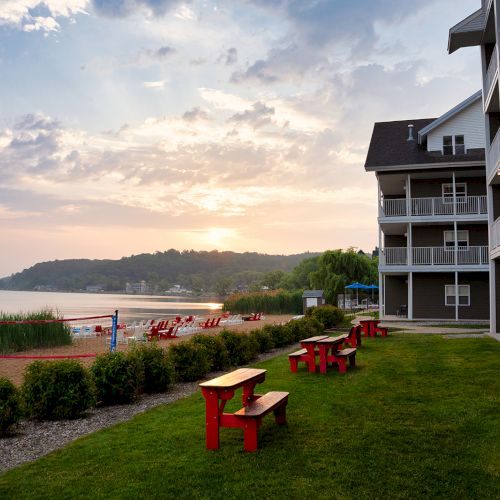 A beachfront scene with red benches, a sandy beach, and a building on the right overlooks a serene water view at sunset.