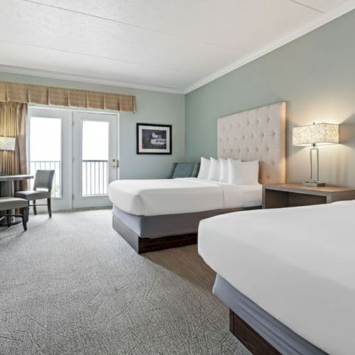 The image shows a hotel room with two beds, a TV, a desk with a chair, and a window with curtains.