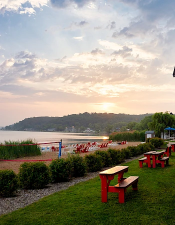 A beachside view with red benches, greenery, and a building at sunset; chairs and water are also visible in the background.