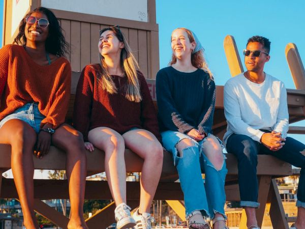 Four people are sitting on a wooden structure outdoors, smiling and enjoying the sunny weather.