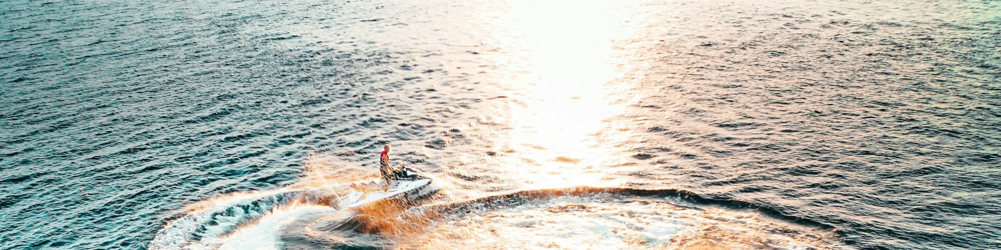 A person is riding a jet ski in circles on the ocean, creating waves under the warm glow of the setting sun.
