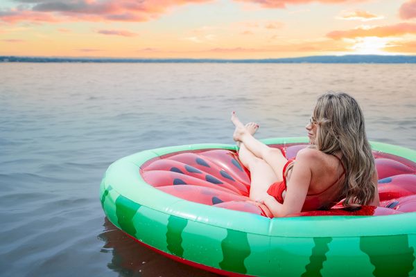 A person relaxes on a watermelon-shaped float in the water during sunset.