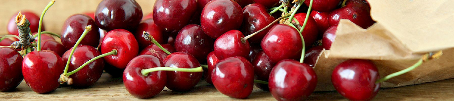 A paper bag spills fresh, red cherries onto a wooden surface, creating a rustic and appetizing scene.