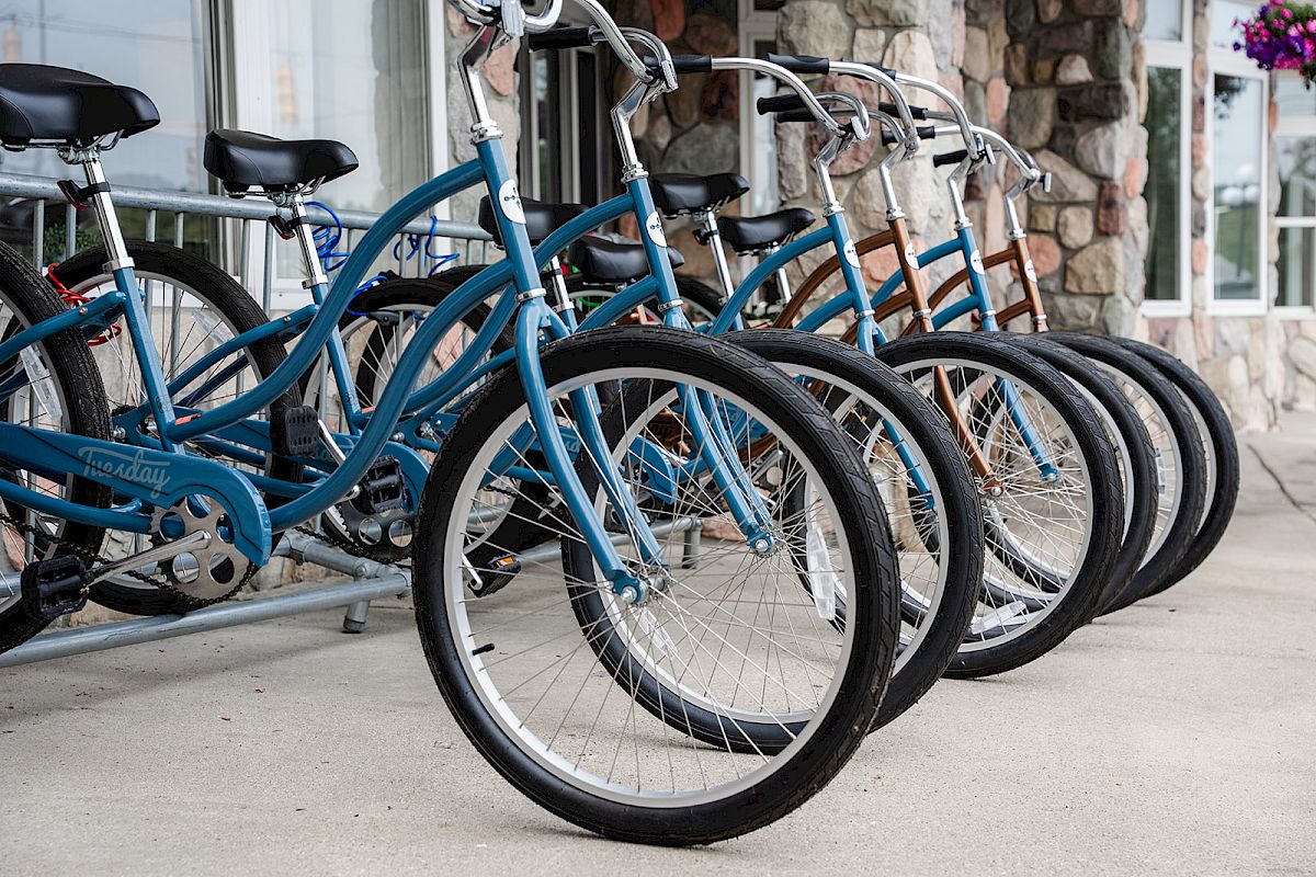 A row of parked blue bicycles with wide handlebars and black tires is lined up against a stone wall on a concrete surface.