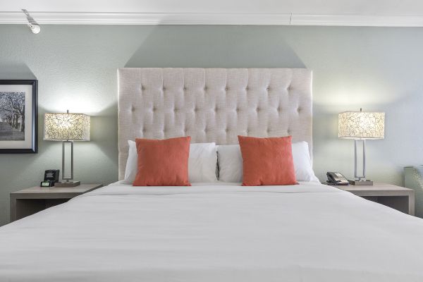 A neatly made bed with a tufted headboard, two orange pillows, flanked by lamps on bedside tables in a bedroom.
