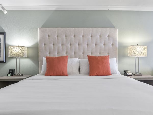 A neatly made bed with a tufted headboard, two orange pillows, flanked by lamps on bedside tables in a bedroom.