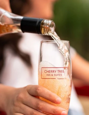 Pouring a drink into a glass labeled &ldquo;Cherry Tree Inn & Suites&rdquo; at a relaxed outdoor gathering, friends in the background.
