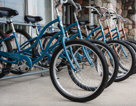 Bikes lined up in a row at a bike rack outside a building, with blue frames and large front wheels.