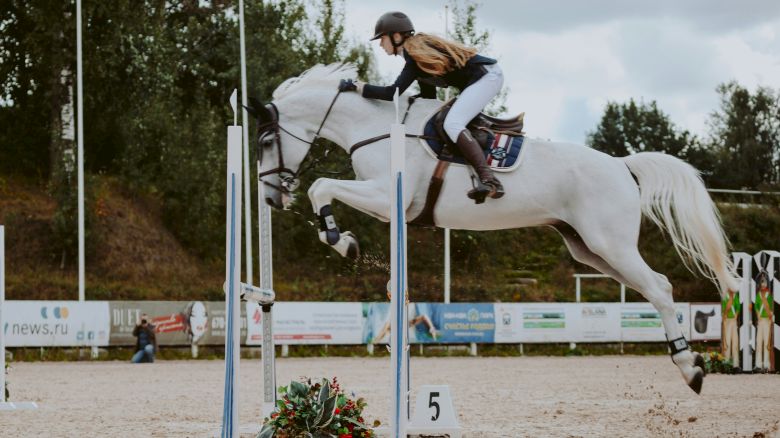 A person is riding a white horse, jumping over an obstacle in an outdoor equestrian setting.