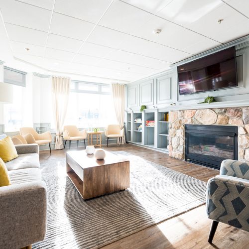 Cozy living room with a stone fireplace, built-in shelves, soft beige sofa set, patterned chairs, and a bright, airy vibe with natural light.