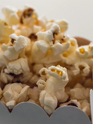 A box full of caramel popcorn, fluffy white kernels with golden crumbs, piled high and spilling over the scalloped edge.