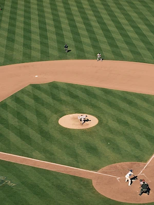 Aerial view of a baseball field: pitcher's mound, infield dirt, pristine green grass with chalk baselines, players scattered around the diamond.