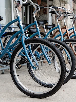 Blue cruisers lined up at a bike rack, front tires facing the camera, parked in a neat row by a building.