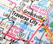 A close-up map shows Traverse City, Michigan with highways, lakes, and nearby towns like Interlochen and Benzie highlighted on the colorful road map.