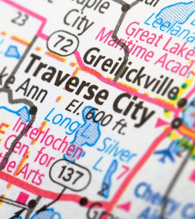 A close-up map shows Traverse City, Michigan with highways, lakes, and nearby towns like Interlochen and Benzie highlighted on the colorful road map.