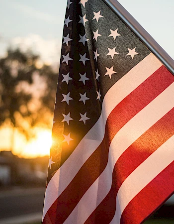 An American flag flutters in the warm sunset, its stars and stripes catching the light as the day fades.