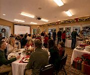 A cozy Christmas dinner buffet in a decorated room, with families gathered around tables and warm lights and gifts.