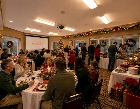 A cozy Christmas dinner buffet in a decorated room, with families gathered around tables and warm lights and gifts.