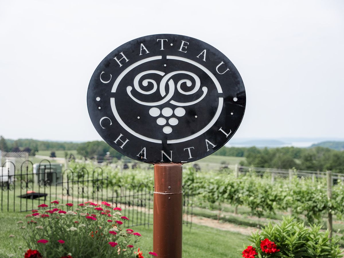 A round metal sign reading &ldquo;CHATEAU&rdquo; with a swirl logo, standing in a landscaped vineyard garden.