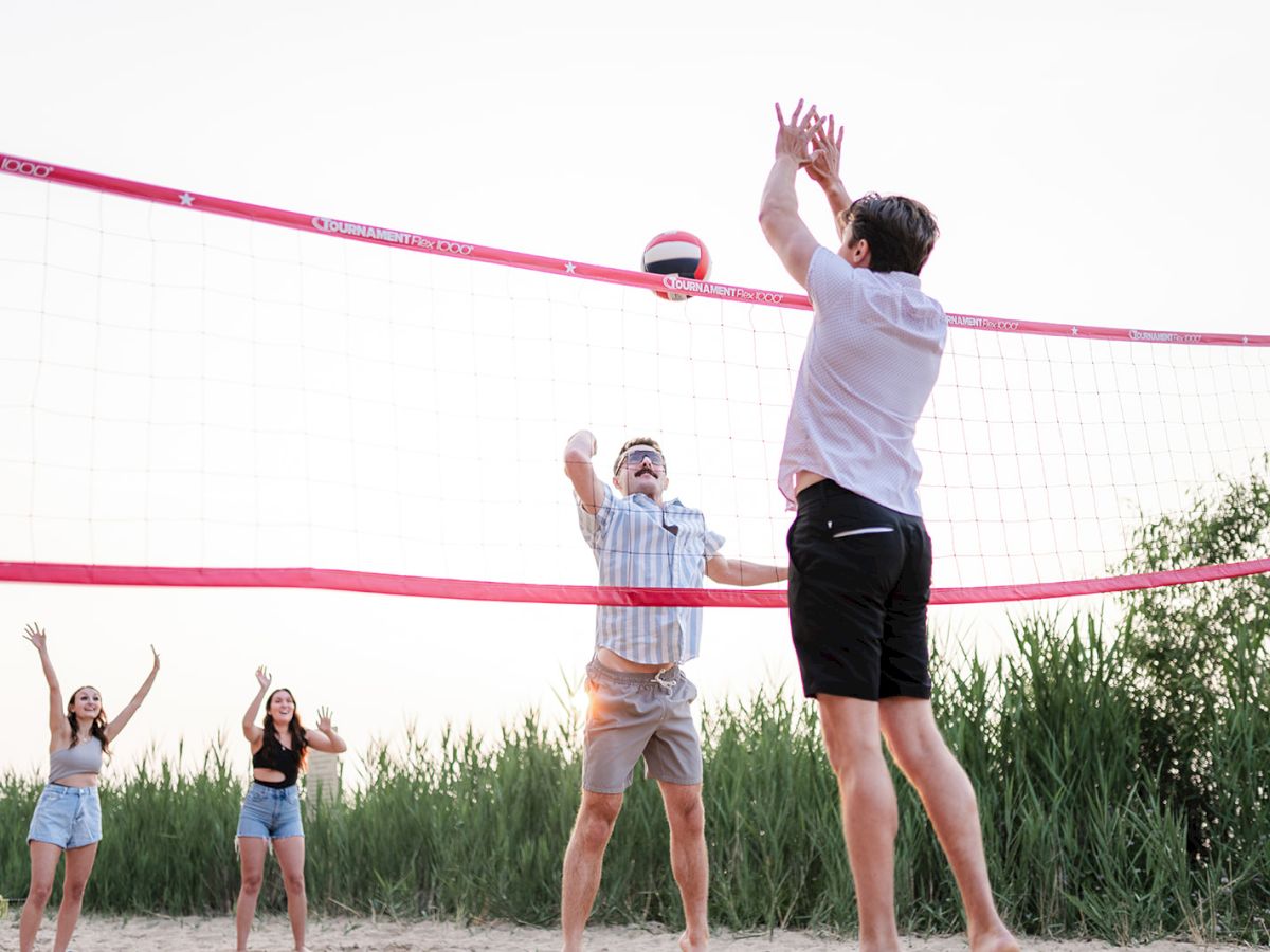 Beach volleyball game as players jump to spike and block the ball over a pink net at sunset.