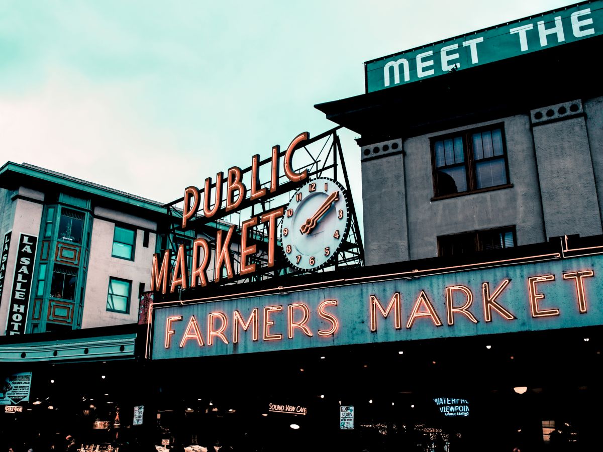 The image shows the iconic neon signs for "Public Market" and "Farmers Market" at the entrance of Pike Place Market in Seattle, Washington.