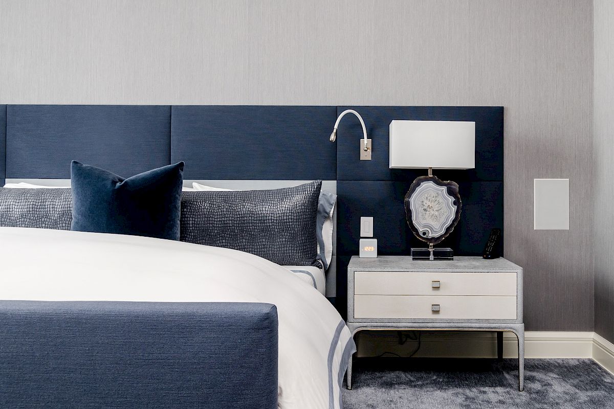 A modern bedroom with a blue and white color palette, featuring a bed, nightstand with a lamp, and decorative pillows, ending the sentence.
